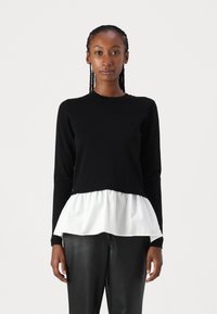 Maglione nero a maniche lunghe con una orlo peplum bianco. Presenta un collo a giro, una consistenza morbida e un top aderente. Abbinato a pantaloni neri in pelle sintetica.