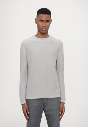 Helles graues Langarmshirt mit einem strukturierten Rautenmuster, rundem Ausschnitt und ribbed Bündchen. Kombiniert mit dunkelgrauen Jeans.