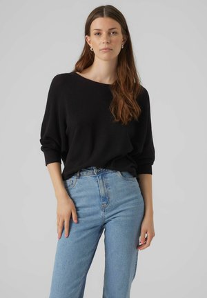 Pull noir en tricot lâche avec un col large et des manches longues, associé à un jean taille haute bleu clair. Design simple et décontracté.