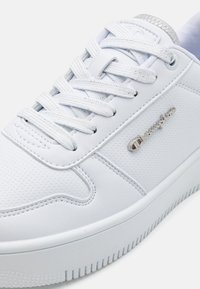 Sneaker in pelle bianca con design forato, lacci piatti e dettagli in metallo argentato. Presenta un collo imbottito e una suola in gomma testurizzata.