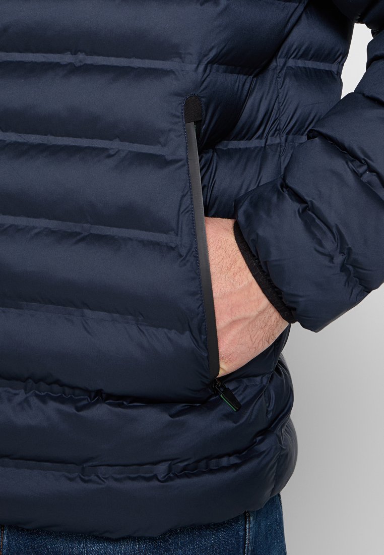 Granatowa kurtka puchowa z poziomym pikowaniem, zamykanymi bocznymi kieszeniami oraz czarnym wykończeniem krawędzi kieszeni. Miękka tekstura materiału.