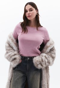 Rosa Kurzarmtop mit Rundhalsausschnitt, kombiniert mit hoch taillierten dunkelblauen Jeans. Ein gestreifter Kunstpelzmantel mit weiten Ärmeln.