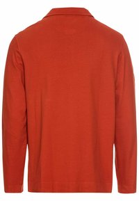 Langærmet skjorte i ensfarvet rust-orange farve. Har en krave, blød stof tekstur, lige snit og minimale syninger.