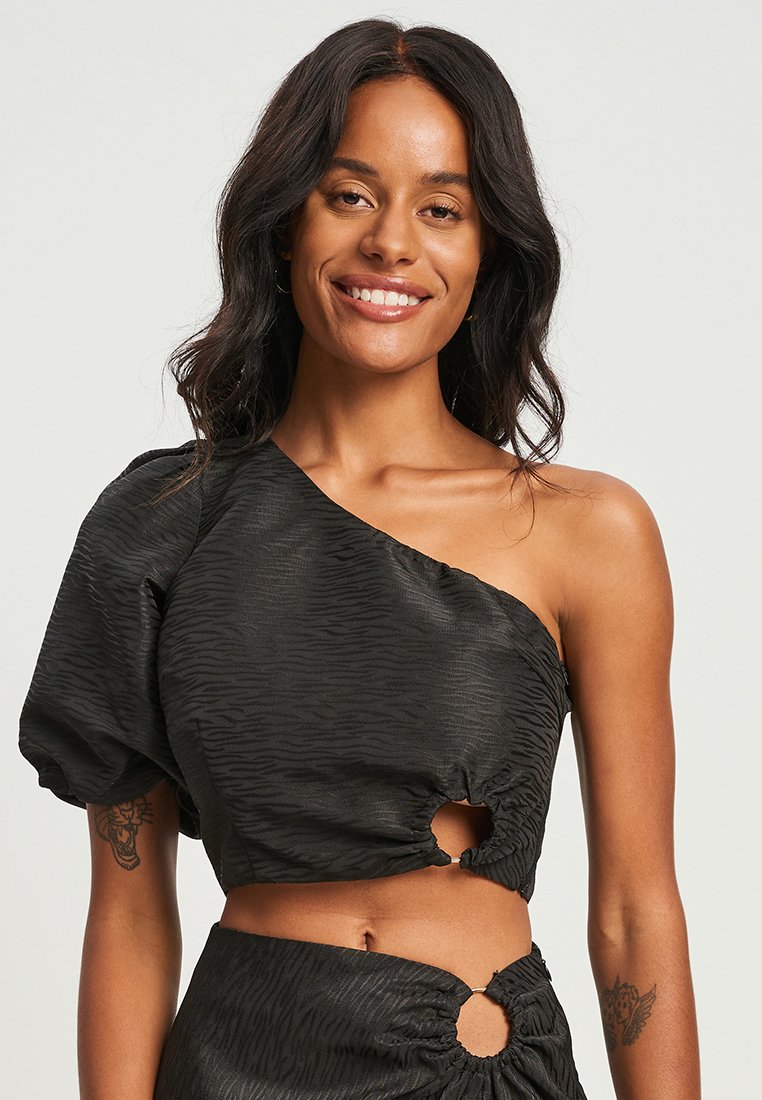 Must have ühes õlas crop-top mustast tekstuuriga kangast, puffvarrukaga ja lõike-detailidega. Omab kogutud vööd ja peent triibumustrit.