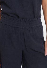 Marineblaue, strukturierte Stoffhosen mit einem elastischen Bund und Rüschendetails an der Taille, die ein lockeres Design bieten.