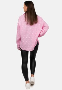 Maglietta rosa a maniche lunghe con motivo a cuori bianche, vestibilità oversize, tessuto texture, abbinata a leggings neri e sneakers bianche.
