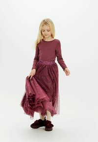 Burgundowa bluzka z długim rękawem zestawiona z wielowarstwową spódnicą z tiulu z kolorowymi plamkami. Stylizację dopełniają ciemne buty z kokardkami.