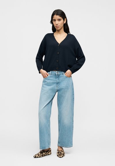 Ναυτικό ζακέτα με V-λαιμόκοψη και κλείσιμο με κουμπιά, συνδυασμένο με ανοιχτό μπλε τζιν παντελόνι φαρδιάς γραμμής. Τα φλατ παπούτσια με animal print ολοκληρώνουν το σύνολο.