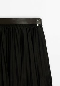 Jupe plissée noire avec une large ceinture en cuir noir maintenue par deux boutons-pression argentés sur fond blanc.