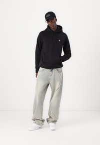 Zwarte katoenen hoodie met een voorzak, gecombineerd met lichtblauwe oversized jeans met een gebogen naad en witte sneakers.