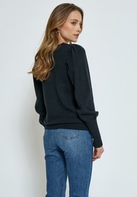 Black knit sweater with puffed sleeves and a ribbed hem, paired with blue jeans featuring back pockets and a slight stretch.