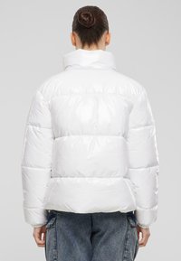 Hvit polstret jakke med en blank finish, med høy krage og lagdelt design. Bak har den en boksformet silhuett og elastiske mansjetter.