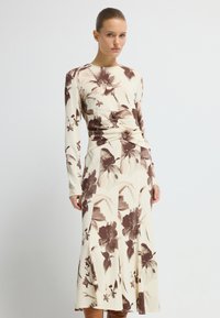 Sukienka z długim rękawem w kremowym materiale z dużymi brązowymi kwiatowymi wzorami. Posiada dopasowaną talię i zwiewną spódnicę, co nadaje jej zorganizowany kształt.