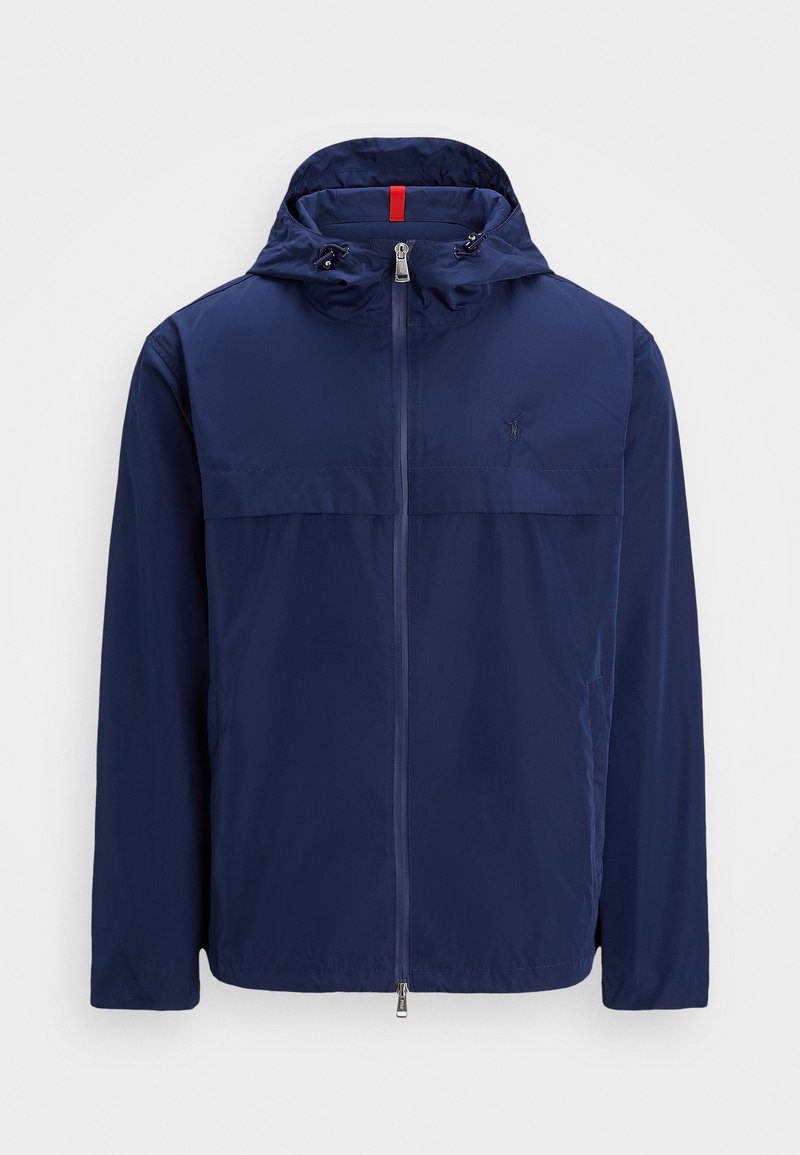 Giacca leggera navy con cappuccio, zip frontale e coulisse. Presenta una cucitura sul petto e un piccolo logo sul lato sinistro. Tessuto liscio e resistente all'acqua.