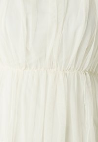 Abito in tulle bianco con vita arricciata, texture a strati e tessuto morbido e trasparente. Delicato e leggero, con un design fluido.