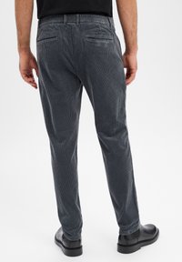 Ciemnoszare spodnie sztruksowe o dopasowanym kroju, z teksturowaną powierzchnią, elastycznym pasem i dwoma tylnymi kieszeniami. Stylizowane z czarnymi butami.