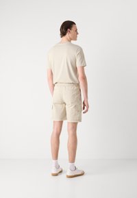 Beige bavlněné tričko a cargo šortky, které mají elastický pas a boční kapsy, doplněné o bílé tenisky a kotníkové ponožky.