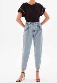 Černé tričko s krátkým rukávem a zipovými detaily, kombinované se světle modrými džíny s vysokým pasem a černými sandály na podpatku.