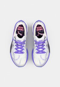 Buty sportowe z białą cholewką, akcentami w kolorze fioletowym oraz teksturowanym wzorem. Fioletowe sznurowadła, logo na języku oraz wzorzysta wkładka.
