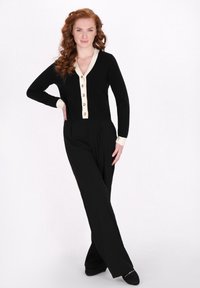 Cardigan negru cu detalii ivory și nasturi aurii, asortat cu pantaloni negri cu talie înaltă. Material neted și croială lejeră.