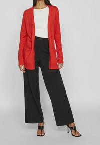 Röd stickad cardigan med öppen front och två fickor, kombinerad med svarta vida byxor och svarta sandaler med remmar.