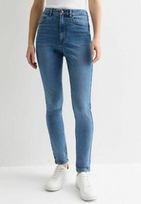 Vaqueros ajustados de mezclilla azul de talle alto con una textura suave y detalles de costura mínimos, combinados con zapatillas blancas.