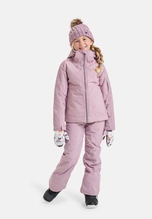 Rosa isolierte Skijacke und -hose mit hohem Kragen. Strickmütze in Pink mit Bommel und gemusterte Handschuhe. Schwarze Schneestiefel.
