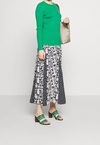 Vihreä ribbineulepaita, kukallinen ja pilkullinen midi-hame, vihreät ja laivastonsiniset lohkokorkoiset sandaalit, kantaen beigeä olkalaukkua.