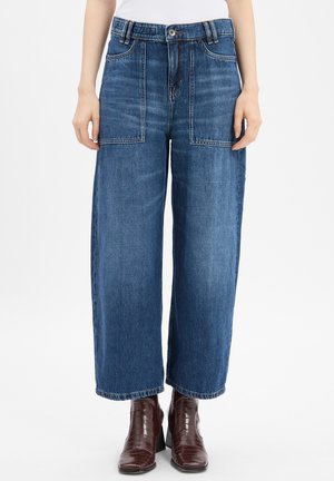 Wijd-uitlopende, mid-blauwe denim jeans met twee grote voorzakken, riemlussen en een ruwe zoom. Gecombineerd met donkerbruine enkellaarsjes.