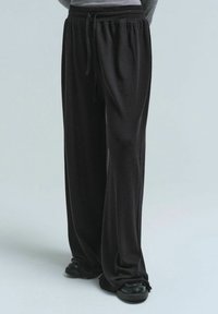 Luftige schwarze Hosen aus weichem Material, mit einem elastischen Bund und Kordelzug sowie einem schmal zulaufenden Bein-Design für optimalen Tragekomfort.
