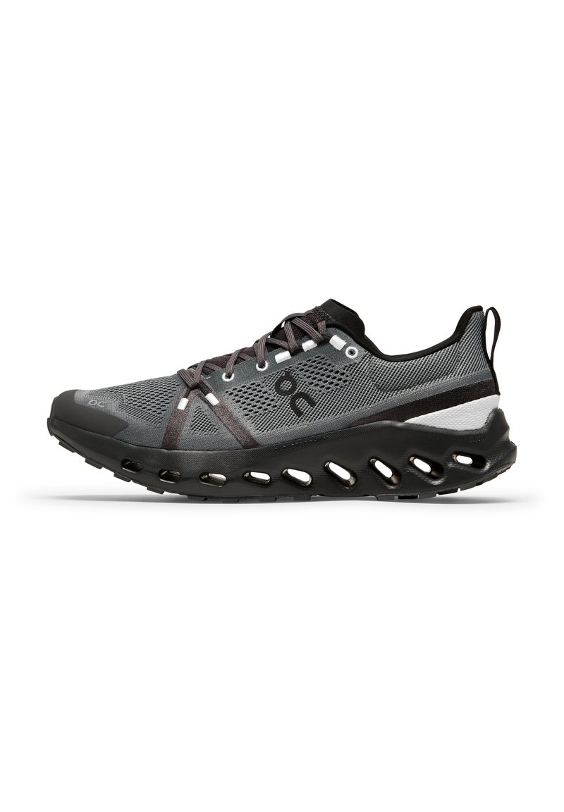 Chaussure de course avec une tige en mesh gris agrémentée d'accents noirs et blancs, une semelle noire flexible avec des perforations de ventilation, et un système de laçage sécurisé.