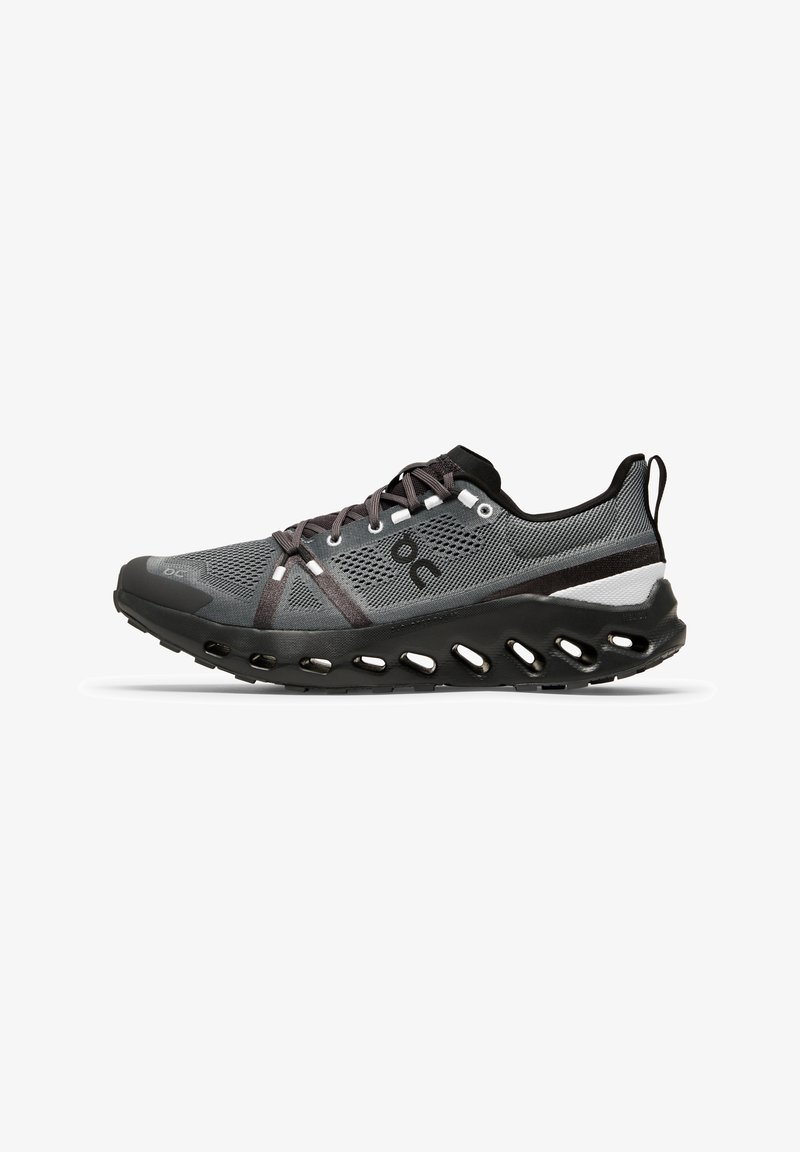 Laufschuh mit einem grauen Mesh-Obermaterial und schwarzen sowie weißen Akzenten, einer flexiblen schwarzen Sohle mit Belüftungsöffnungen und einem sicheren Schnürsystem.