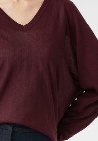 Burgundowy top z dekoltem w serek, z długimi, bufiastymi rękawami oraz elastycznymi mankietami. Lekki, miękki materiał o lekko przezroczystej fakturze.