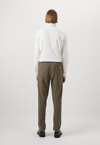 White long-sleeve shirt with a high collar, paired with olive-green pants. The pants feature a relaxed fit and elastic waistband. Black shoes visible.