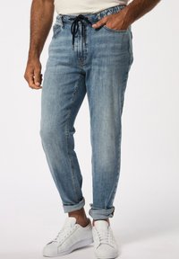 Pantalones jogger de mezclilla de color azul claro con cintura elástica y cordón, con puños enrollados y combinados con zapatillas blancas.