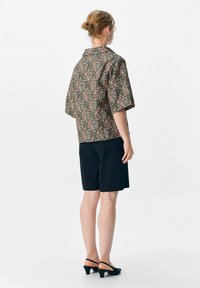 Blouse à manches courtes à motifs floraux sur fond noir ; associée à un short noir ajusté et des chaussures à talons ouverts noires. Tissu lisse avec une coupe décontractée.