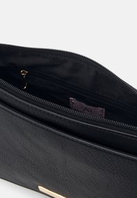 Sac à main en cuir noir avec fermeture éclair, présentant une texture lisse, des poches intérieures et un accent de quincaillerie dorée.