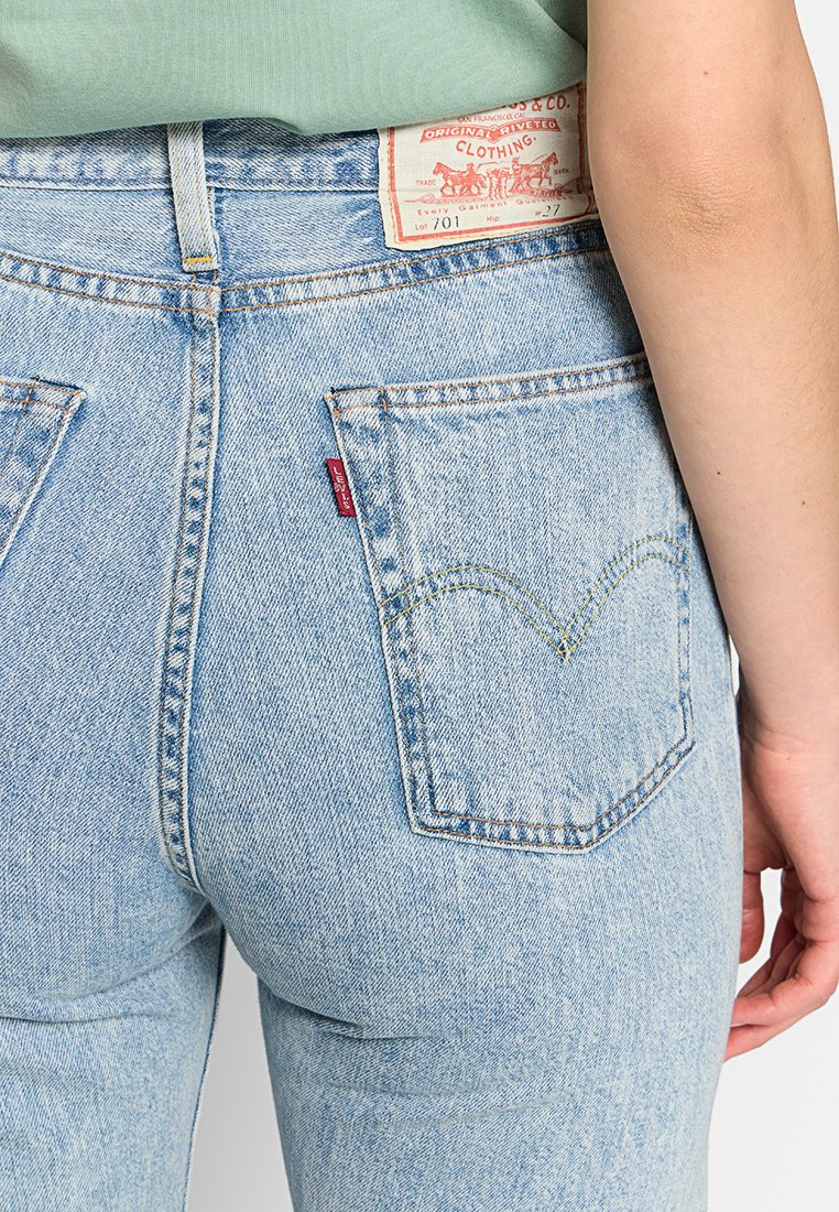 Jean en denim bleu clair à taille haute, avec une patch en cuir à l'arrière, des coutures jaunes et des poches arrière classiques au design iconique.