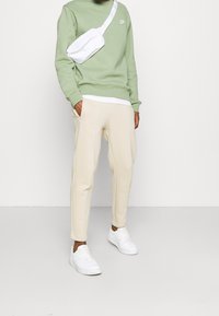 Ljusgrön sweatshirt med en vit Nike-logotyp, kombinerad med krämfärgade tapered sweatpants och vita sneakers. En vit axelremsväska fulländar looken.