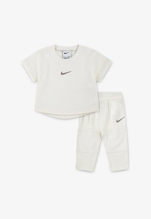 Kremfarget Nike T-skjorte med korte ermer og nettingtekstur, kombinert med matchende bukser med elastisk midjebånd og logoaksenter.