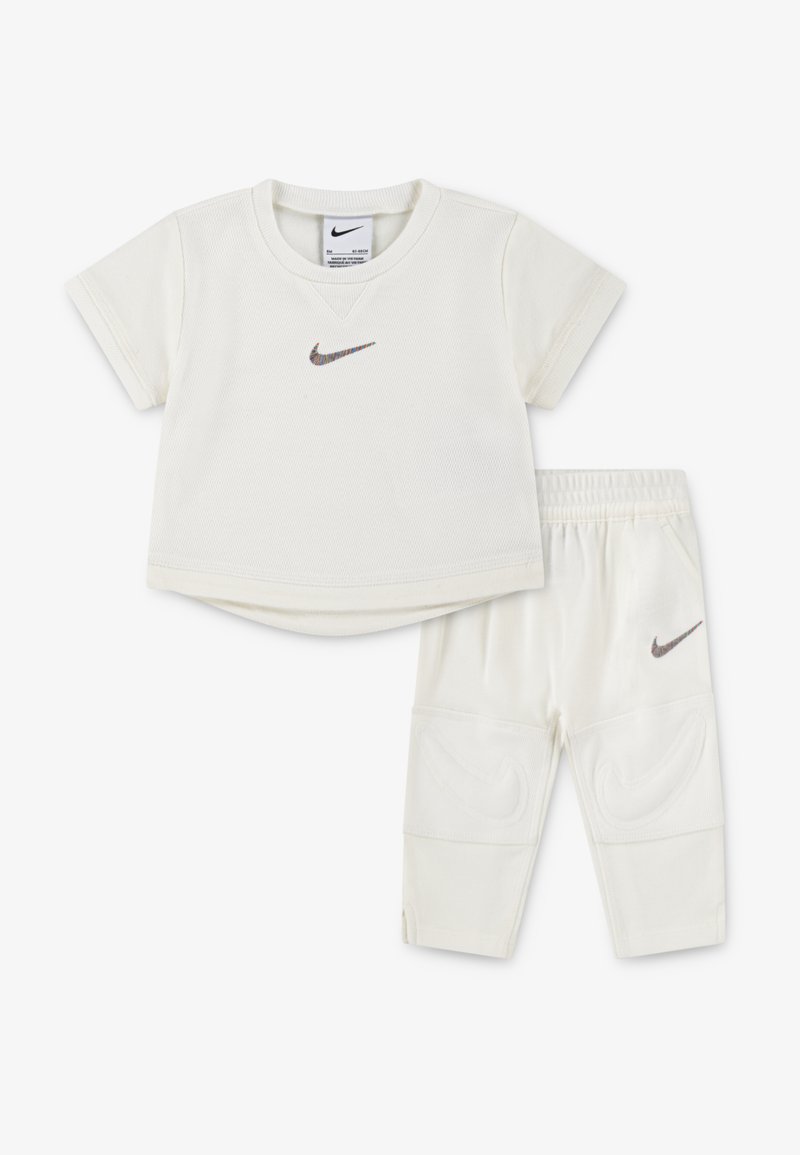 Kremfarvet Nike t-shirt med korte ærmer og meshstruktur, kombineret med matchende bukser med elastisk taljebånd og logo-detaljer.