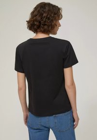 T-shirt nera in cotone con maniche corte e scollatura rotonda. Texture liscia e vestibilità rilassata, mostrata su una persona di spalle.