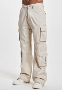 Pantaloni cargo beige in cotone, con multiple tasche laterali, una vestibilità rilassata e un design a gamba dritta. Tessuto semplice, senza motivi visibili.