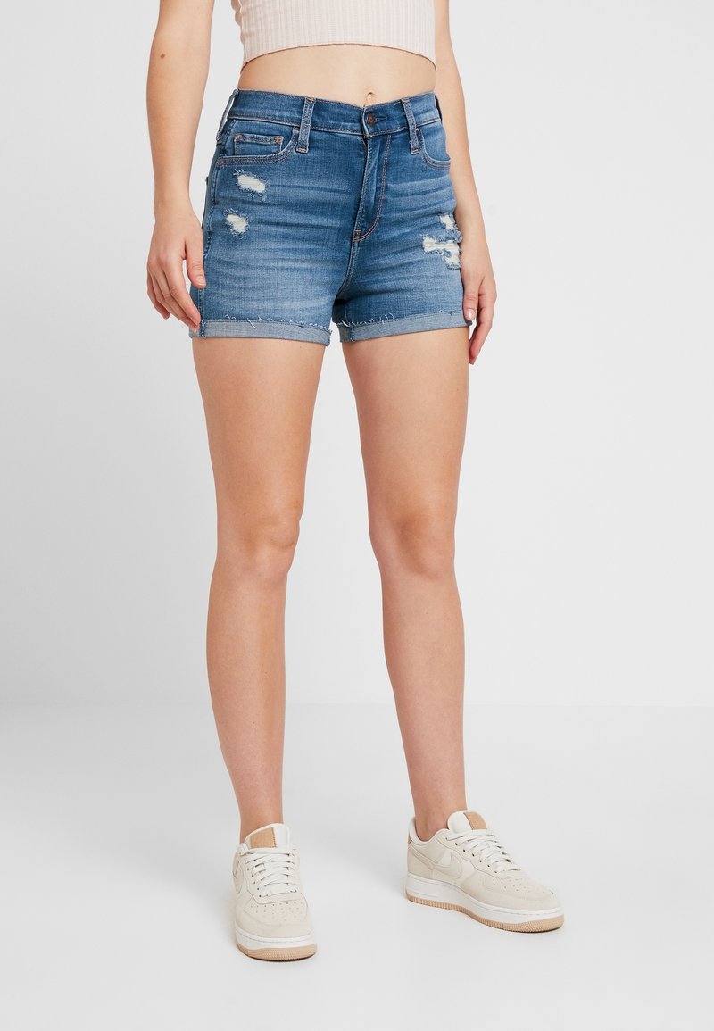 Denim shorts in a light blue wash, featuring frayed hems and distressed detailing. Paired with white sneakers for a casual look.