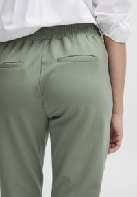 Zielone dresowe spodnie z elastycznym paskiem w talii, o gładkiej teksturze, z dwoma naszytymi kieszeniami z tyłu i luźnym krojem.