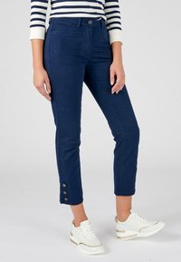 Navyblauwe cropped broek met een getailleerd ontwerp en vijf zakken, met knoopaccenten bij de enkels. Gecombineerd met witte sneakers.