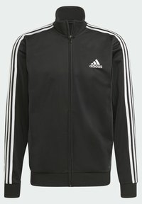 Veste de survêtement Adidas noire avec trois bandes blanches sur les manches, fermeture éclair complète à l'avant et logo Adidas sur la poitrine gauche.