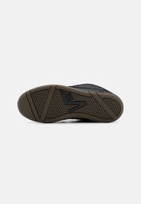 Adidași negri cu un superior din țesătură texturată, talpă din cauciuc cu modele hexagonale de aderență și un accent distinctiv al logo-ului.
