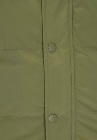 Olivgrüne Steppjacke im Nahaufnahme, mit glatter Textur, Druckknöpfen und vertikalen Steppnähten. Leichtes und isoliertes Design.