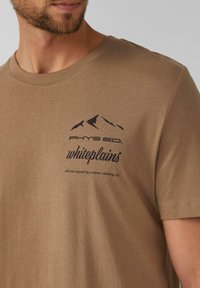 Braunes Kurzarm-T-Shirt aus weichem Stoff mit einer schwarzen Berg-Grafik und dem Text "PHYS ED. whiteplains" auf der Brust.